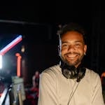 A cheerful man wearing headphones poses confidently in a modern gaming studio.