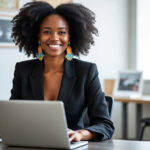 Black female founder smiling in a modern office while working on a laptop
